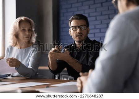 Serious engaged business startup leader man speaking to colleagues at team meeting, explaining details, ideas for project, sitting at table, brainstorming with group Royalty-Free Stock Photo #2270648287