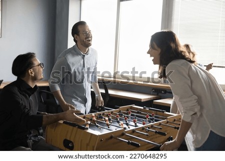 Joyful excited millennial couple of colleagues competing in table soccer on work break, laughing out loud at board game. Office friends playing tabletop football, having fun Royalty-Free Stock Photo #2270648295