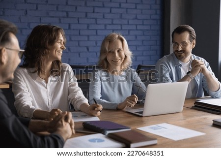 Positive senior mentor woman training employees, interns, laughing with staff, joking at conference table. Different aged team of happy colleagues brainstorming on meeting Royalty-Free Stock Photo #2270648351
