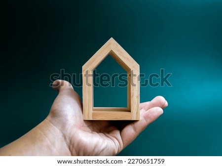 Home, house, family, real estate, property concepts. Minimal miniature wooden small house with empty space inside for text or logo in human hand holding isolated on blue background.