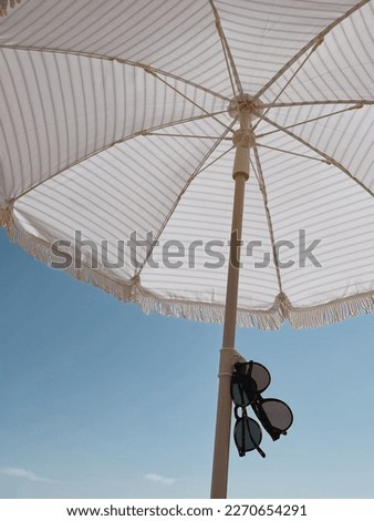 Sunglasses and beach umbrella over blue sky. Minimal summer travel vacation concept. Chilling, relaxin, lounging on the beach