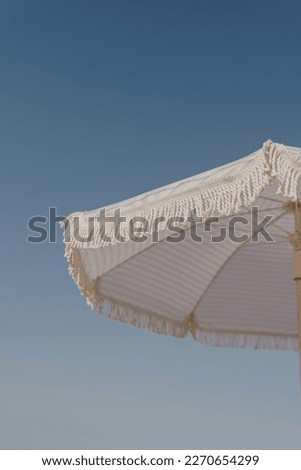 Aesthetic summer vacation concept. Striped beach umbrella and blue sky. Minimal luxury holidays composition Royalty-Free Stock Photo #2270654299