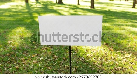Closeup white metal sign at green grass background, nameplate with a space for your text. Horizontal banner