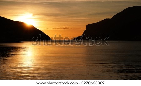 The silhouette of kayak set against an amazing golden sunset overlooking the mountains around the fjord in the Vágar island, Faroe Islands