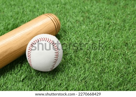 Wooden baseball bat and ball on green grass, closeup. Space for text