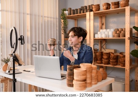 A young Asian man entrepreneur live streaming to sale craft products  to customers in his shop , Technology online business concept.
