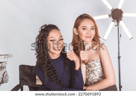 Two congenial and attractive asian models making a thumbs up sign. During a break time at a studio.