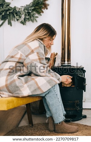 Young caucasian woman sitting in living room near fireplace in country house and warms his hands.