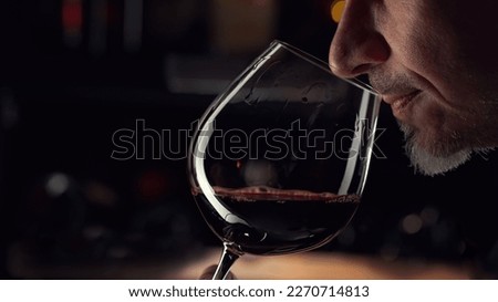 Close up man smelling red wine in wine glass. Wine expert tasting, rating and drinking wine, bottles in background.