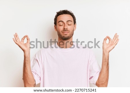 Closeup portrait of young handsome male keeps eyes closed gesturing hands in meditation yoga pose relaxing in zen isolated over white background enjoys the silence makes stress reducing techniques  Royalty-Free Stock Photo #2270715241