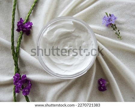 Picture taken from above of a cream plastic container placed over some white clothes forming a spiral around it and some flowers around it  