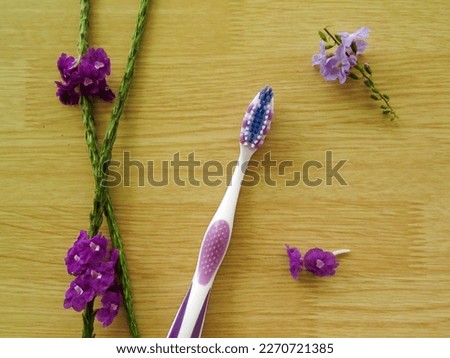 Picture of a white blue and purple toothbrush placed on a wood background and surrounded by some small purple flowers. Picture taken from above 