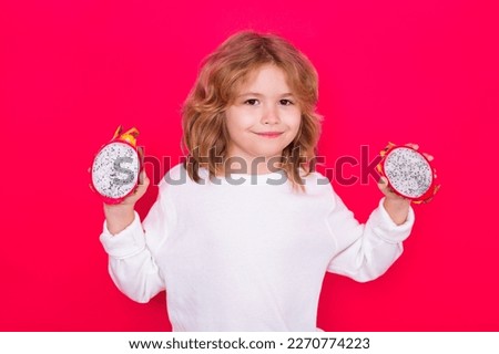 Kids face with fruits. Kid hold dragon fruit in studio. Studio portrait of cute child with dragon fruit isolated on red background.