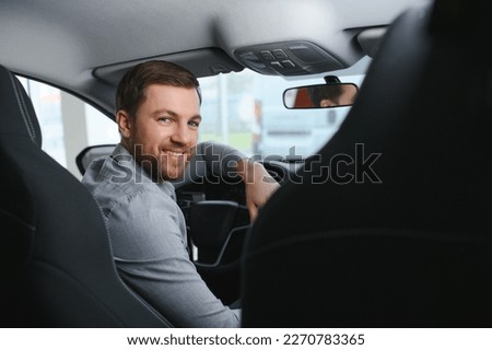 Taxi driver smiling while turning over to the backseat looking talking with clients. Successful businessman husband looking at the backseat at dealer shop before buying a car. Royalty-Free Stock Photo #2270783365