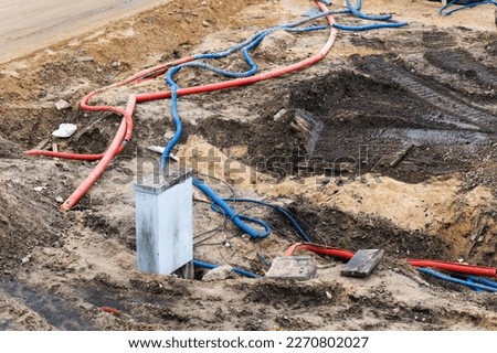 Construction site landscape. Heavy machinery imprint. Dried mud vehicle wheel shape. Red and blue plastic pipe. Electrical wires protector. Plastic cover for electrical wires and cables background. 