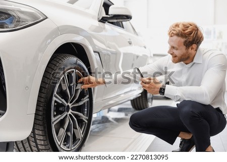 Man customer male buyer client in shirt take photo of wheel disc mobile cell phone choose auto want buy new car automobile in showroom salon vehicle dealership store motor show indoor Sales concept.
