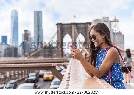 Phone. New York City woman using phone app walking on Brooklyn Bridge by Manhattan city skyline. Young female professional multicultural lady wearing sunglasses, New York City, USA.