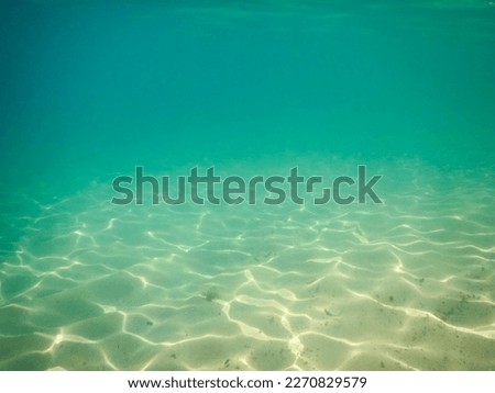 Beach sand under water with reflections of light on the rippled surface of the sea. Water in shades of green and turquoise blue.