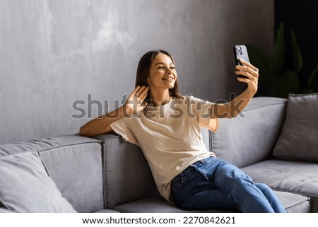 Young woman taking selfie with her cellphone while sitting at living room.