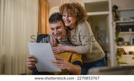 Young man and his mother woman hold paper read good news in letter sit at desk at home beautiful female received correspondence bank statement or notification invitation scholarship pleasant message Royalty-Free Stock Photo #2270853767