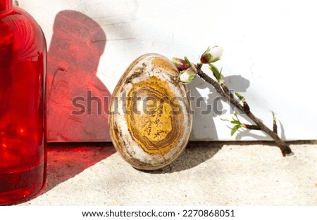 Easter egg with natural stone texture. Spring still life with a blooming tree branch in a small red glass vase against white wall background. Cinematic vintage authentic Easter holiday photo. 