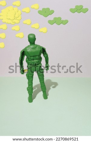 A green soldier on a two-color background holds a yellow heart in his hand. Clouds and a yellow sun. Conceptual idea.