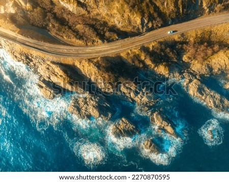 Aerial view of road, rocky sea coast with waves and stones at sunset in Lofoten Islands, Norway. Landscape with beautiful road, transparent blue water, rocks. Top view from drone of highway in summer Royalty-Free Stock Photo #2270870595
