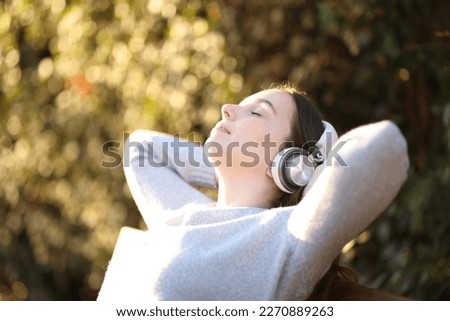Woman resting listening to music sitting on a bench in a park