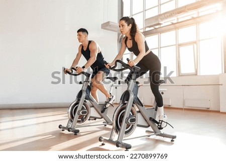 beautiful athletic couple of cyclists train in the fitness room on static bicycle simulator, man trainer and fitness woman go in for sports together on simulators in the morning in bright room Royalty-Free Stock Photo #2270899769