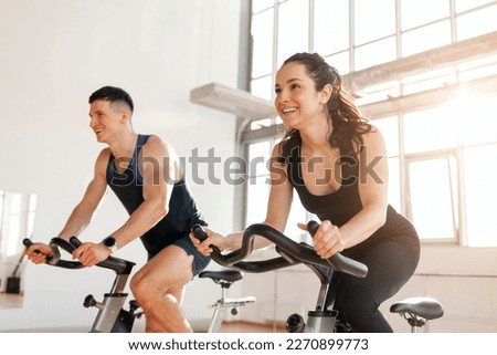beautiful athletic couple of cyclists train in the fitness room on static bicycle simulator, man trainer and fitness woman go in for sports together on simulators in the morning in bright room Royalty-Free Stock Photo #2270899773