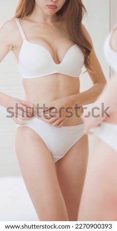 close up view - asian woman wearing underclothes is standing in front of mirror and dissatisfied about her body shape Royalty-Free Stock Photo #2270900393