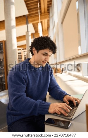 Dark-haired positive Latin young man, using laptop, doing researches on internet, typing text on keyboard, communicating online. People. Education. Business. Remote job and modern technology concept Royalty-Free Stock Photo #2270918497