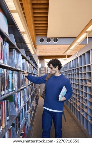 Smart Latin American male student, standing by bookshelves in university library campus and choosing books, searching informations for hi diploma project. Learning. Education. Educated people concept
