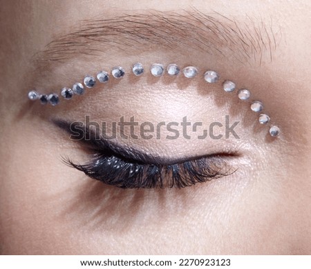 Closeup macro shot of human female closed eye with unusual makeup. Woman with rhinestones arrows on eyelid. Royalty-Free Stock Photo #2270923123