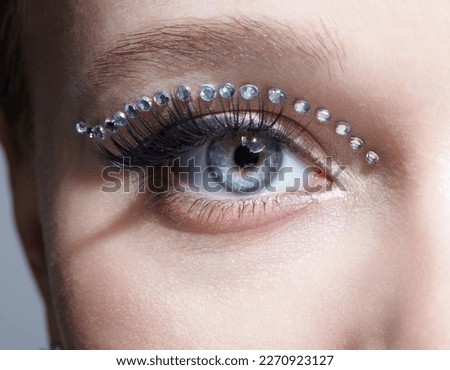 Closeup macro shot of human female eye with unusual makeup. Woman with rhinestones arrows on eyelid. Royalty-Free Stock Photo #2270923127