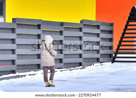 A woman walks along a decorative fence on a winter day