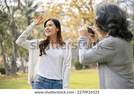 Happy Asian grandma taking a picture of her beautiful granddaughter with a retro camera while strolling in the green park together. Happy family and leisure concept