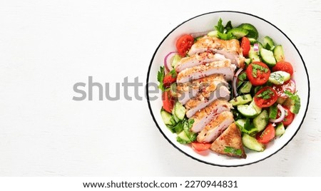 Grilled chicken breast, fillet and fresh vegetable salad of lettuce, arugula, spinach, cucumber and tomato on a white background. Healthy lunch menu. Diet food. Top view. Panorama with copy space.
