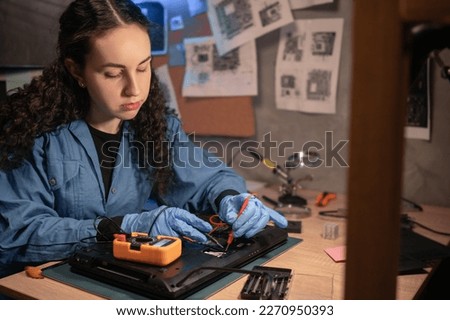 Concentrated female technician busy repairing laptop and it testing with multimeter at retro workshop. Concept of professional worker and repair service. Royalty-Free Stock Photo #2270950393
