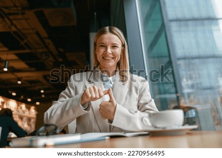 Smiling businesswoman communicating in sign language while looking at camera while sitting in cafe