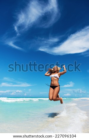 Young latin woman in the bikini jumping at the tropical beach.Copy space