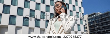 Attractive young businesswoman in white suit talking phone standing near business centre
