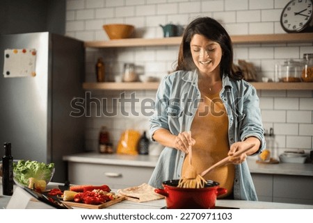 Beautiful pregnant woman preparing delicious food. Smiling woman cooking pasta at home. Royalty-Free Stock Photo #2270971103