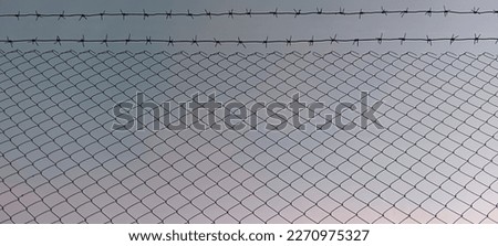 Coiled razor wire with its sharp steel barbs on top of a mesh perimeter fence ensuring safety and security, preventing access or the escape prisoners, blue sky background