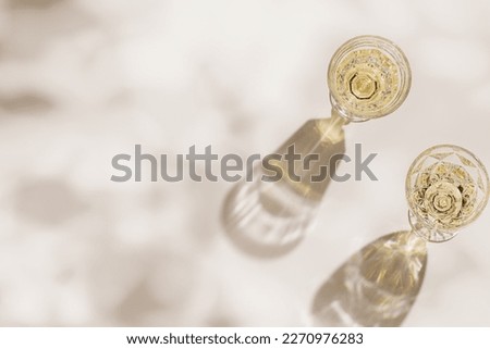 Top view of wineglasses with white wine, leaves shadow and glare from glass at sunlight, summer alcohol drink background beige monochrome, creative aesthetic view of wine glass goblets style on table