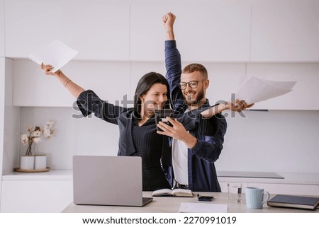 Excited caucasian couple after calculate their year earnings, celebrating successful business at new home using calculator, laptop. Woman raises hands in winner gesture holds papers. Financial freedom Royalty-Free Stock Photo #2270991019