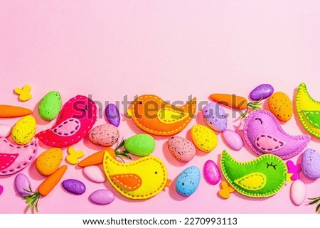 Handmade Easter background with colorful felt birds. Decorative eggs and sweet candies, cute rabbits. Hard light, dark shadow, pink backdrop, top view, flat lay