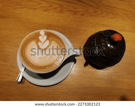 A cup of coffee with a chocolate muffin next to it