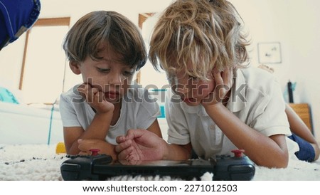 Excited brothers looking at tablet screen lying down together. Portrait of kids watching media online smiling