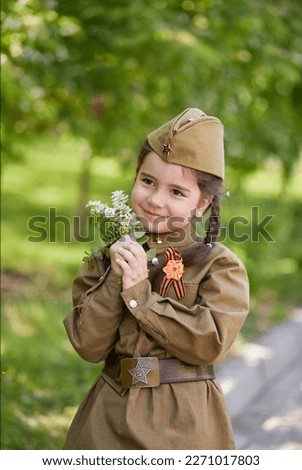 Portrait of a cute little girl in uniform with flowers on a green background. Victory Day, May 9 holiday.
